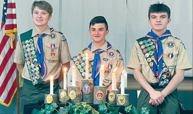 From left, Jack Pfeffer, Camren Ferri and Connor Cooper pose with their red, white and blue Eagle
Scout neckerchiefs and badges. (by the candles and logs symbolizing their trial to Eagle)